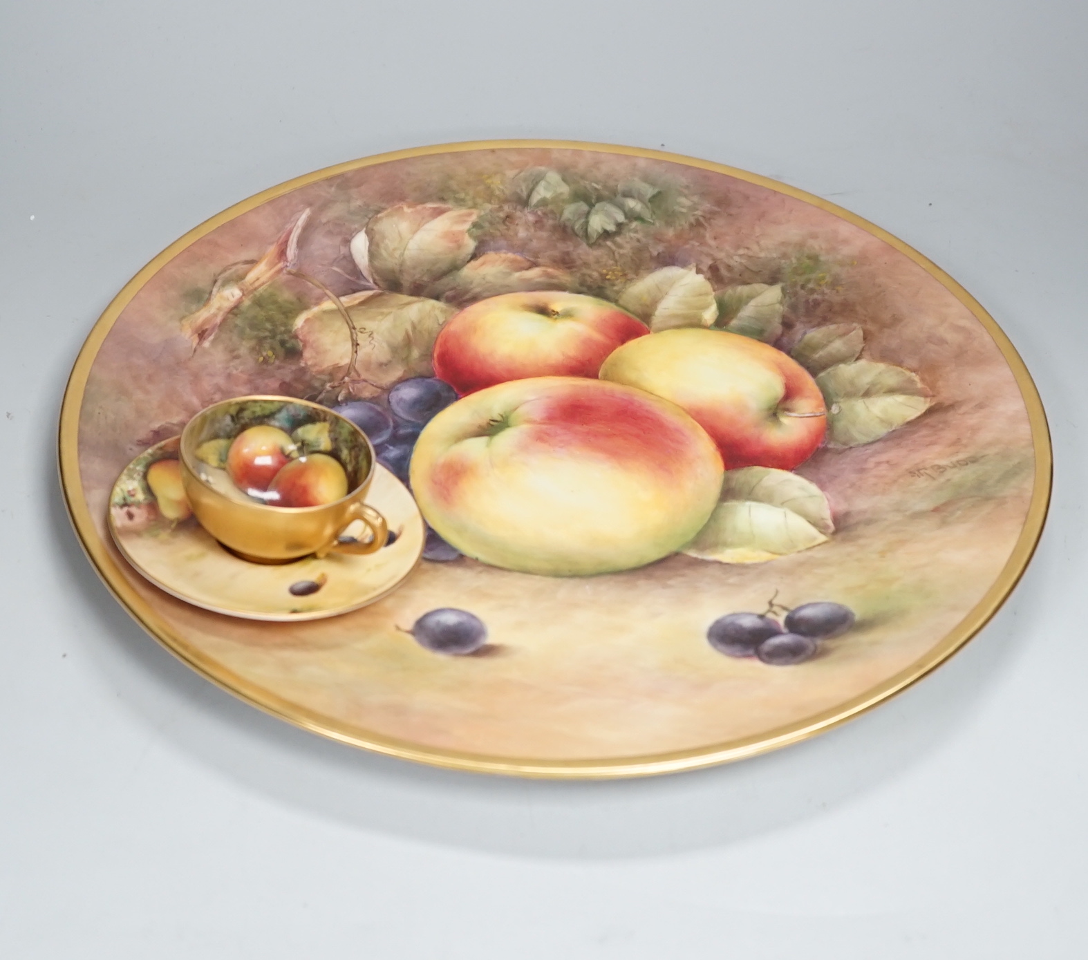 A large fruit painted dish by R. Budd and a Royal Worcester fruit painted miniature tea cup and saucer painted by F Harper and W H Austin, largest 32cm in diameter